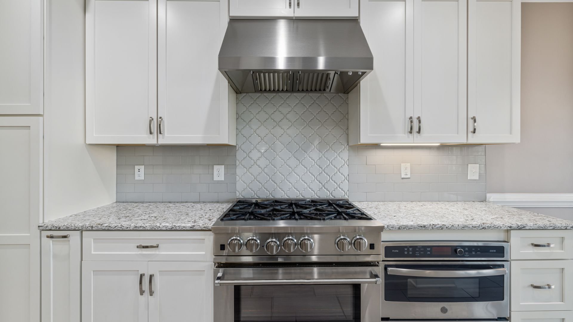Modern kitchen with white cabinets, stainless steel appliances, and arabesque backsplash